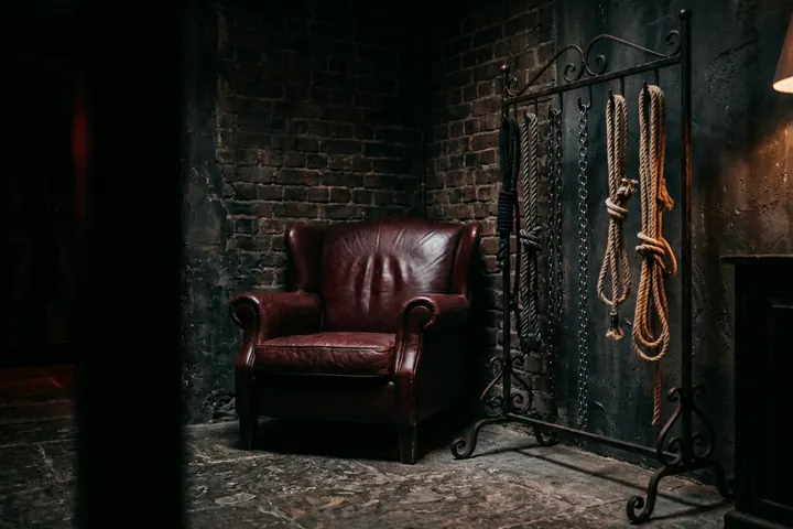 Salon feutré au mobilier de cuir, cordes et chaînes soigneusement rangées, éclairées d'une lumière basse